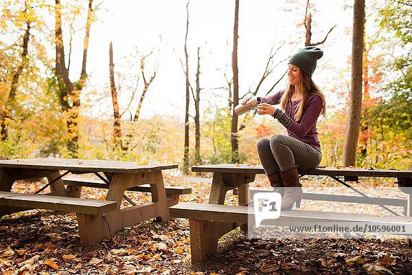 Junge Frau beim Ausgießen von Getränken auf der Picknickbank im Herbstwald