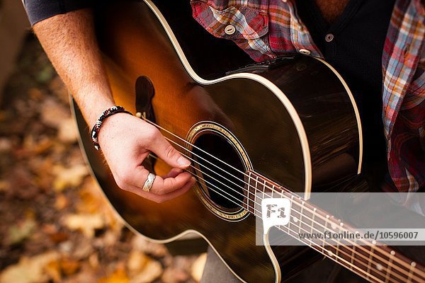 Ausschnitt eines jungen Mannes  der im Herbstwald Gitarre spielt.