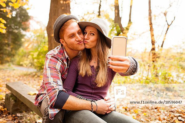 Young couple on bench taking smartphone selfie in autumn forest