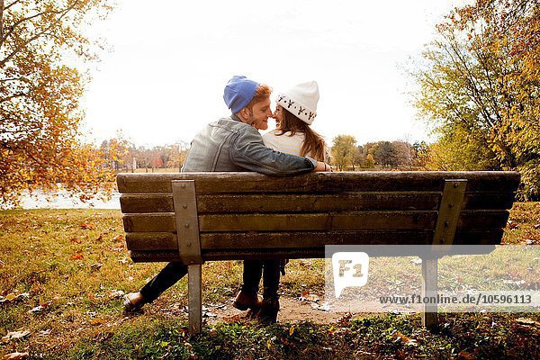 Rückansicht des romantischen jungen Paares auf der Parkbank am Seeufer