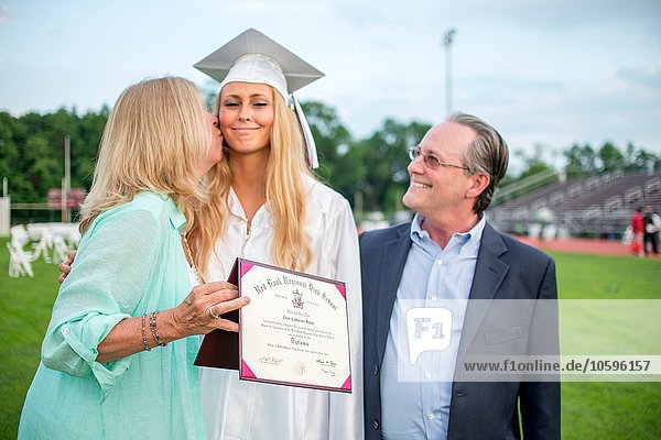 Mother kissing graduate daughter at graduation ceremony