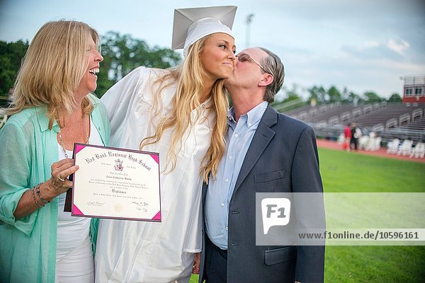 Father kissing graduate daughter at graduation ceremony