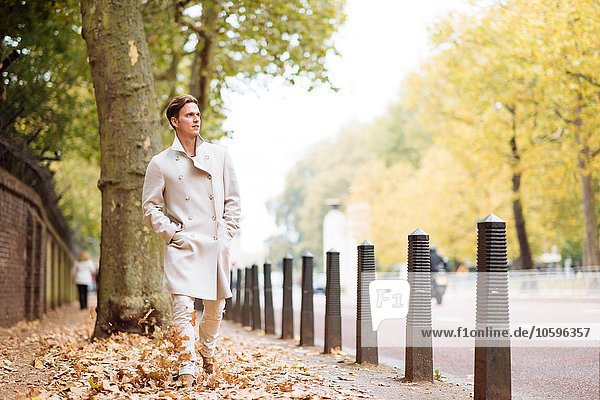 Stilvoller junger Mann beim Spaziergang durch das Herbstlaub im Stadtpark