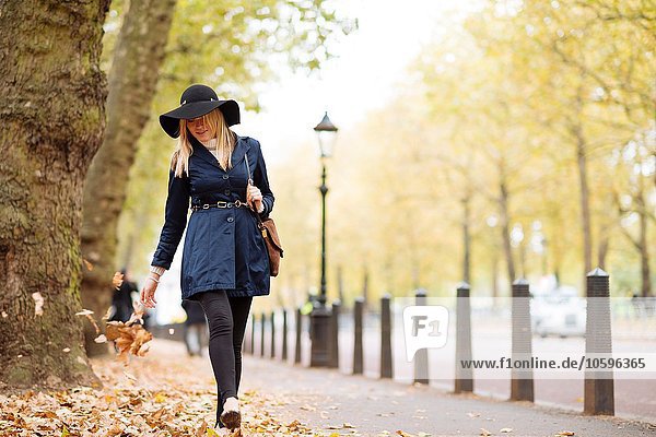 Stilvolle junge Frau beim Spaziergang durch das Herbstlaub im Stadtpark
