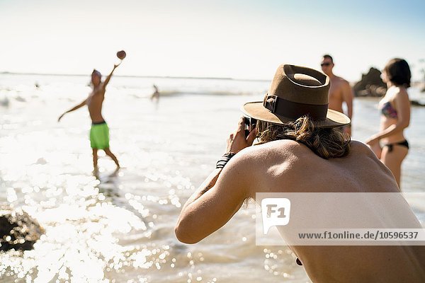 Young man photographing friends playing American football in sea at Newport Beach  California  USA