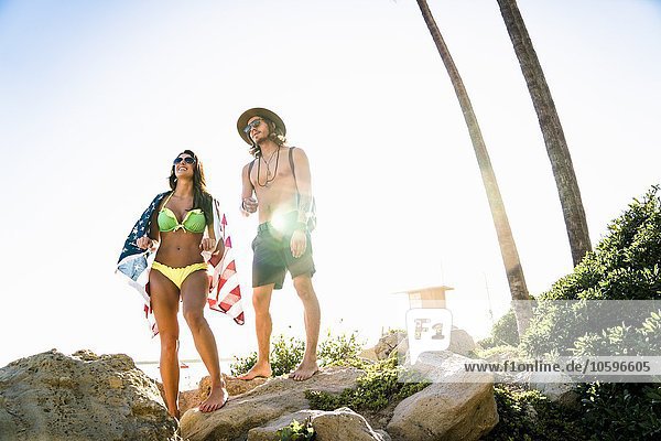 Young couple wrapped in American flag looking out from rocks on Newport Beach  California  USA