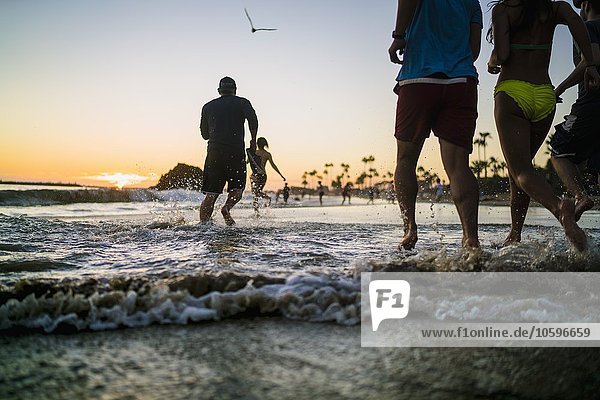 Rückansicht von erwachsenen Freunden  die bei Sonnenuntergang im Meer laufen  Newport Beach  Kalifornien  USA