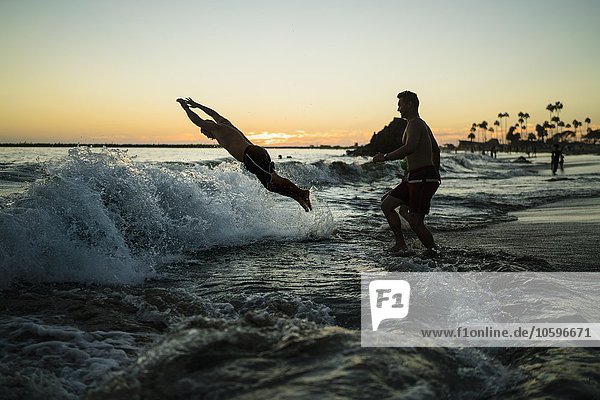 Junge Männer tauchen bei Sonnenuntergang ins Meer  Newport Beach  Kalifornien  USA
