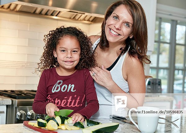 Mother helping daughter chop vegetables in kitchen  looking at camera smiling