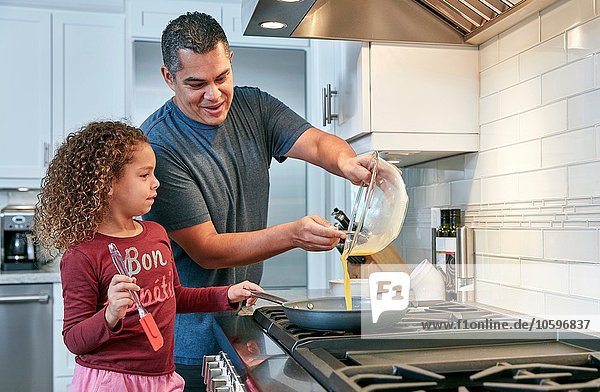 Vater hilft Tochter kochen Omelette auf dem Herd in der Küche  Gießen Ei in die Pfanne