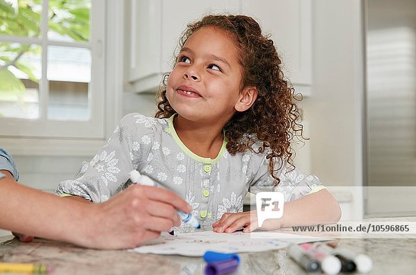 Girl at kitchen counter using felt tip pen to draw picture  looking up smiling
