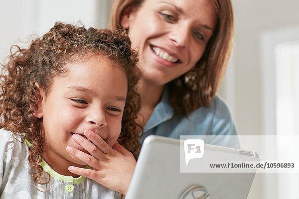 Low angle view of mother and daughter using digital tablet  hand over mouth smiling