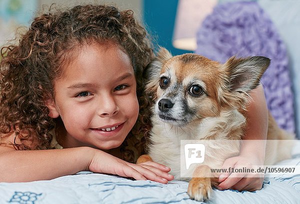 Girl lying on bed arm around dog  looking at camera smiling