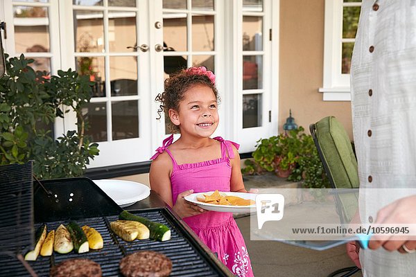 Girl on patio holding plate being served barbeque food by father