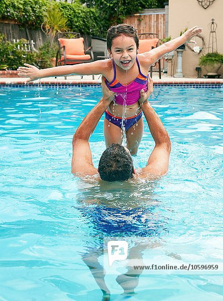 Father in swimming pool lifting up daughter  arms open looking at camera smiling