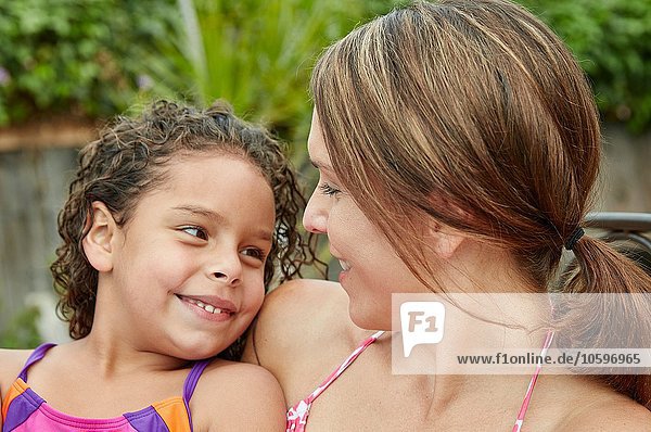 Head and shoulders of mother and daughter wearing swimwear face to face smiling