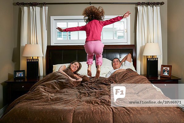 Rear view of girl in mid air jumping on parents bed