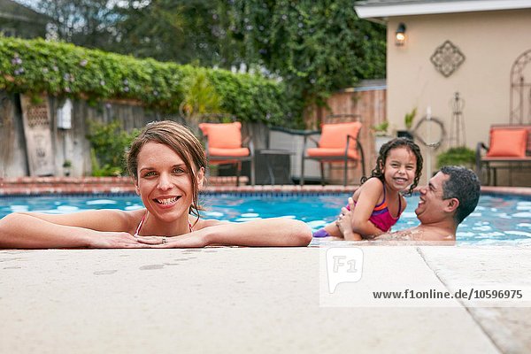 Kopf und Schultern einer erwachsenen Frau mit Familie im Pool  die lächelnd auf die Kamera blickt.