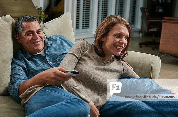 Couple snuggling on sofa  looking away using remote control smiling