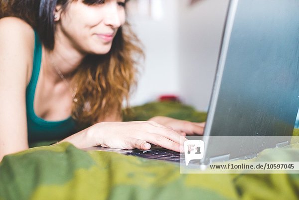 Junge Frau auf dem Bett liegend mit lächelndem Laptop  Differentialfokus
