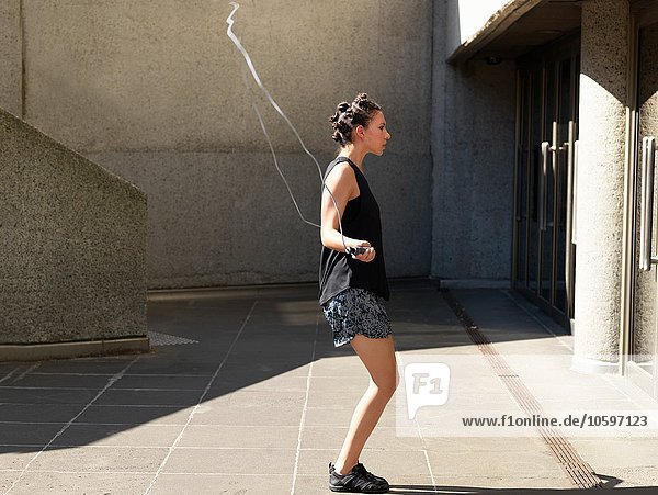 Young woman skipping beside building