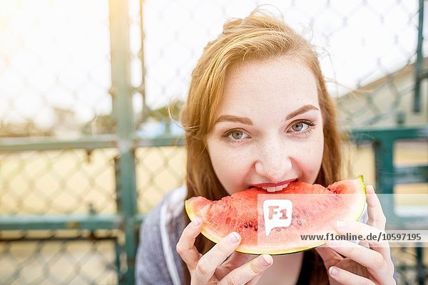 Junge Frau isst Wassermelone neben Sportplatz  London  UK