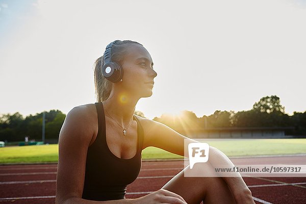 Young female runner on race track listening to headphones