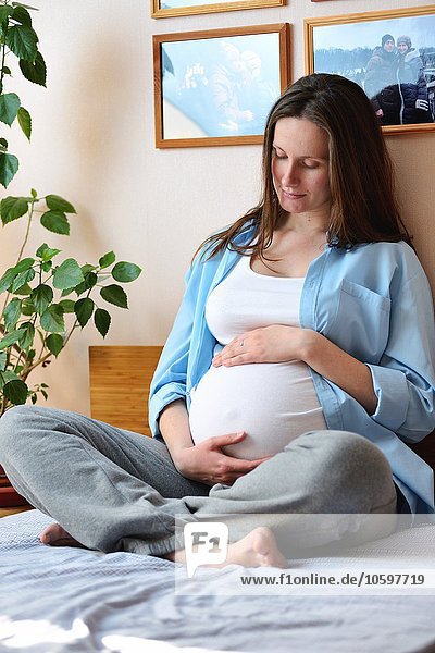 Pregnant woman sitting on bed  holding stomach