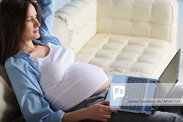 Schwangere Frau auf dem Sofa sitzend  mit Laptop
