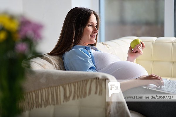 Schwangere Frau auf dem Sofa sitzend  mit Laptop