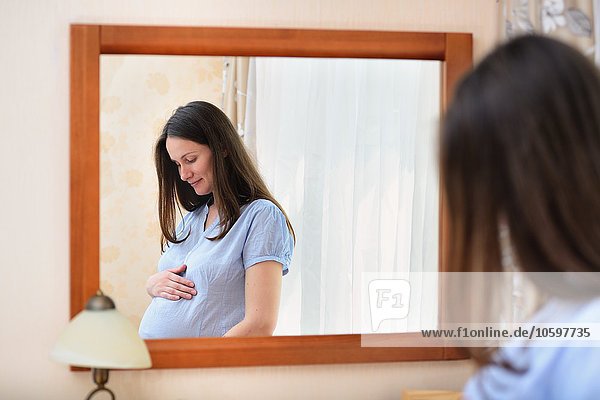 Schwangere Frau  die den Bauch hält  vor dem Spiegel stehend
