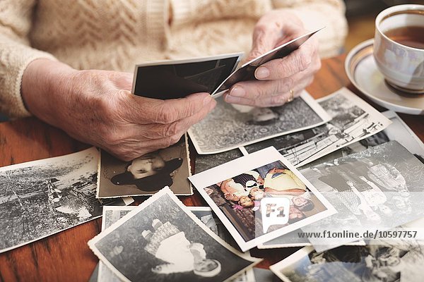 Senior woman sitting at table  looking through old photographs  mid section