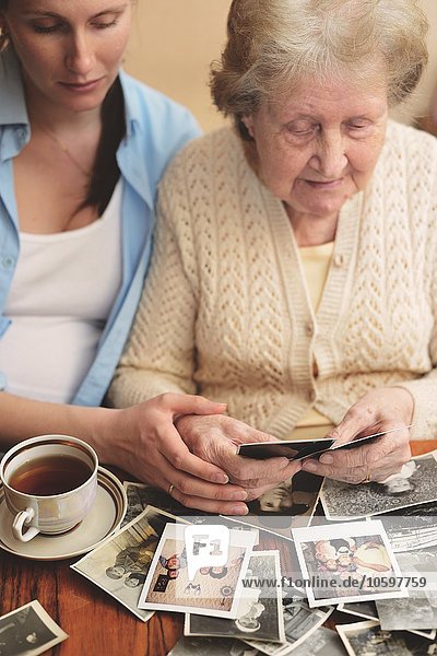 Seniorin und Enkelin sitzen am Tisch und sehen sich alte Fotos an.