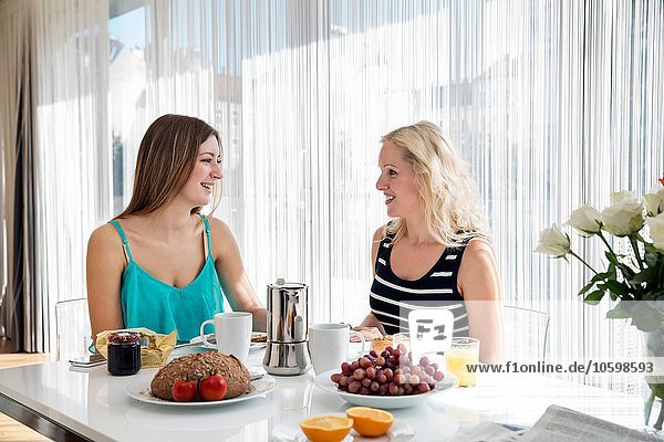Women sitting at dining table enjoying a continental breakfast together  face to face smiling