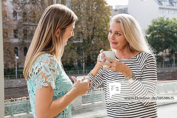 Frauen im Freien mit Kaffeetassen von Angesicht zu Angesicht lächelnd