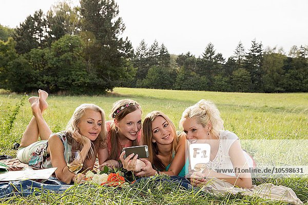 Frauen liegen auf der Vorderseite auf Gras mit dem Smartphone  um Selfie lächelnd zu nehmen.