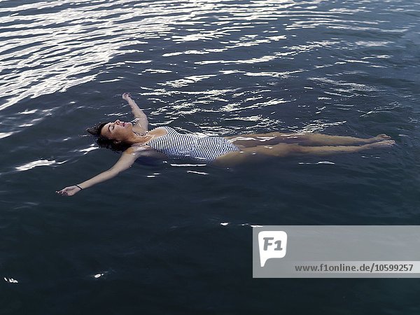 High angle view of woman floating on back in water arms outstretched looking up