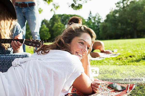 Erwachsene Freunde spielen Akustikgitarre auf dem Teppich auf der Sunset-Park-Party