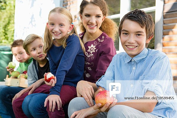 Porträt von Teenagern und Kindern  die auf der Terrasse sitzen und Äpfel essen.