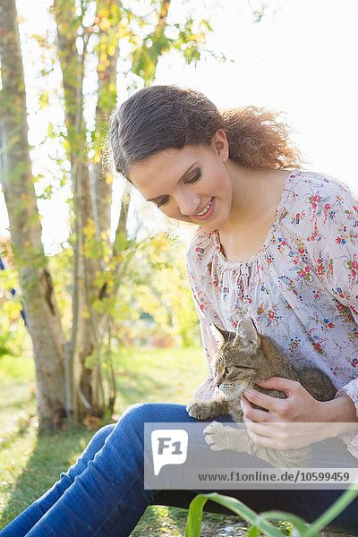 Teenage girl relaxing in garden petting cat