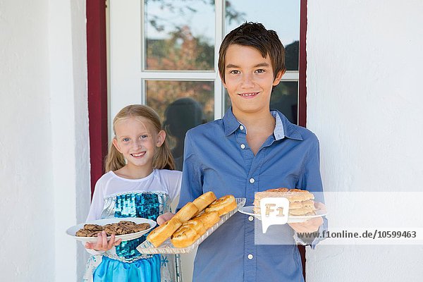 Portrait of teenage boy and sister carrying cakes on patio
