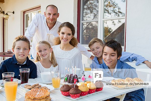 Porträt eines erwachsenen Mannes und einer Familie mit Geburtstagskuchen am Tisch auf der Terrasse