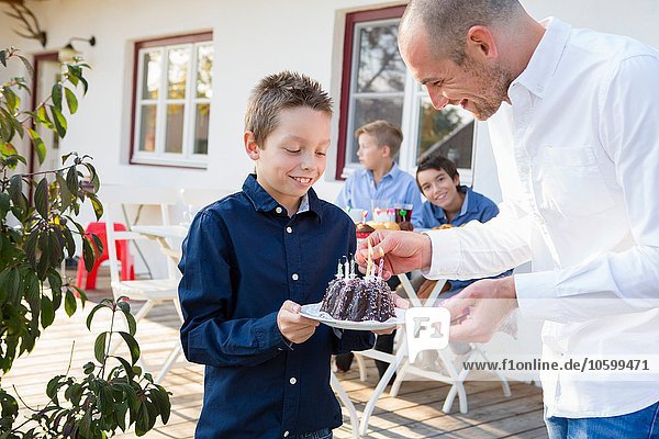 Mid adult man lighting sons birthday cake candles on patio
