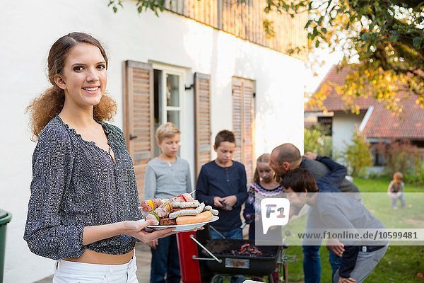 Portrait of teenage girl carrying plate of barbecued food at garden barbecue