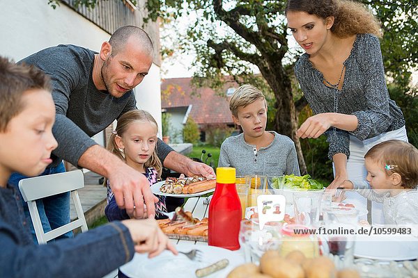 Father and teenage girl helping children at garden barbecue table