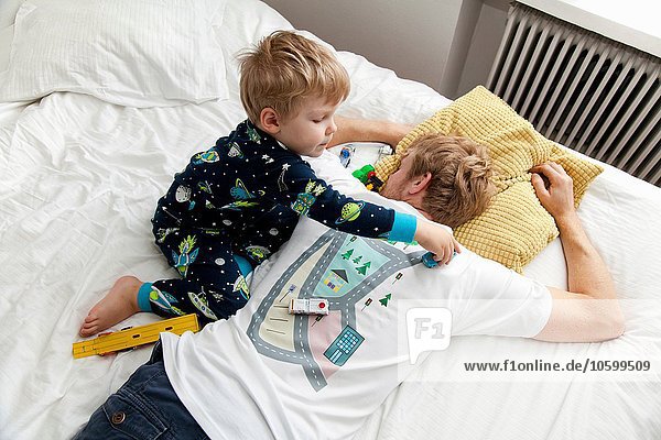 Young boy playing with toy car on back of fathers tshirt in bed