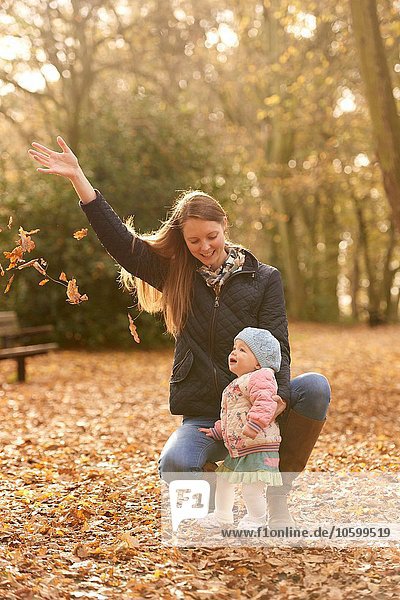 Mittlere erwachsene Frau und kleine Tochter beim Beobachten von Herbstblättern im Park