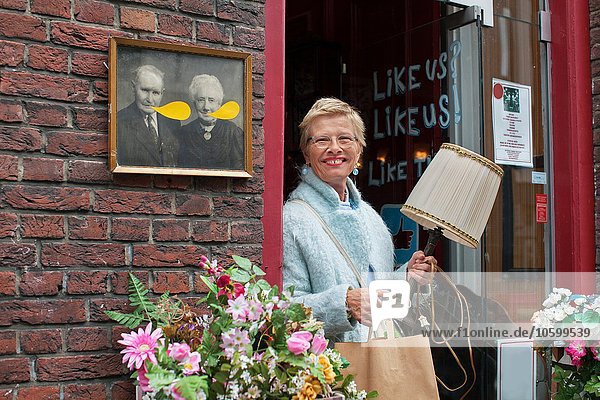 Reife Kundin mit Lampe und Einkaufstasche vor dem Vintage-Shop