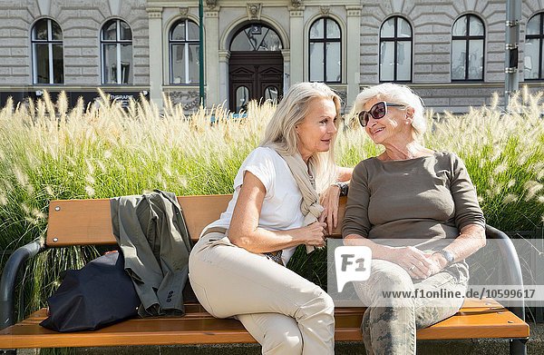 Mother and daughter sitting on bench together  outdoors