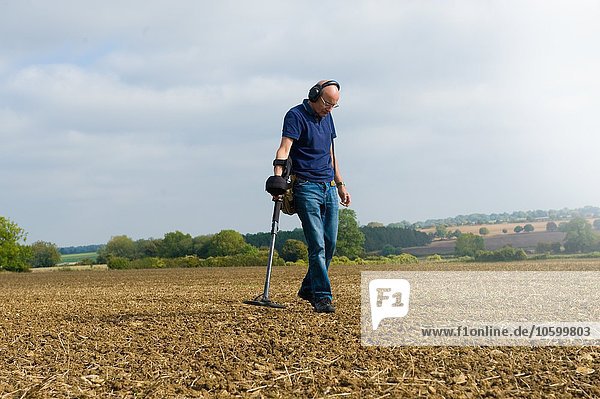 Mature man wearing headphones searching muddy field using metal detector